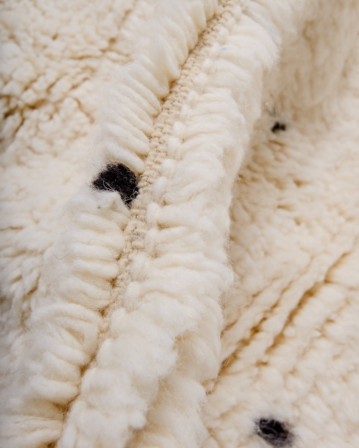 Detail of cream wool rug showing the density of the wool and black strands that make up the polka dots.